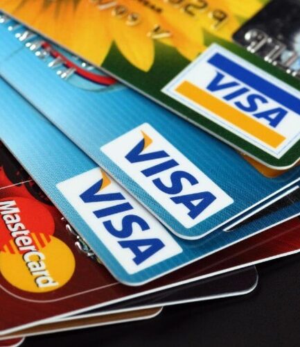 Stack of overlapping credit cards, with Visa logos prominently visible on blue cards and Mastercard logos on other cards nearby.