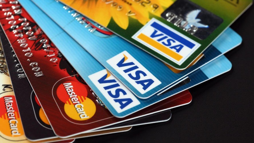 kredi-karti Stack of overlapping credit cards, with Visa logos prominently visible on blue cards and Mastercard logos on other cards nearby.