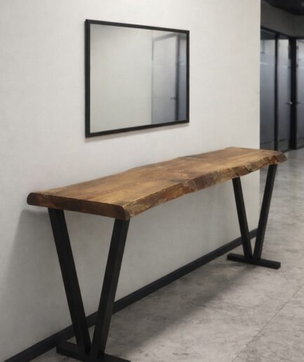 Live-edge wooden bench with black metal V legs against a white wall in a hallway, mirror above it.