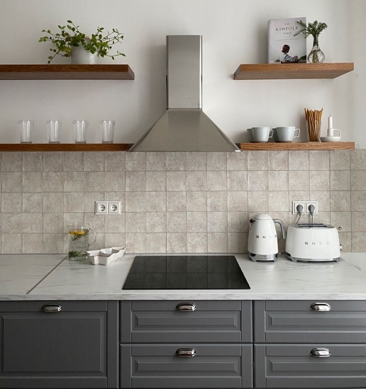 yuzen-raf-ucan-raf Modern kitchen with stainless range hood, gray cabinets, and tiled backsplash; open shelves hold plants, glassware, and small appliances.