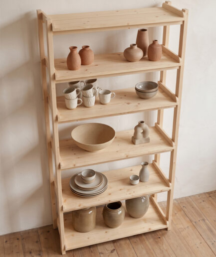Wooden shelving unit against a white wall displaying ceramic vases, bowls, and mugs on the shelves.