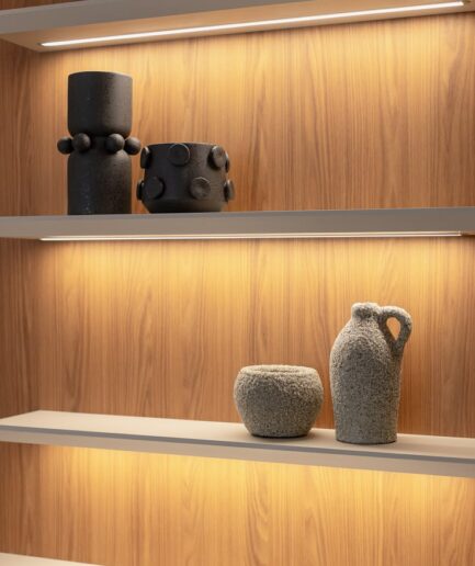 Textured gray ceramic pitcher and small bowl on a white shelf against warm wood paneling with backlighting
